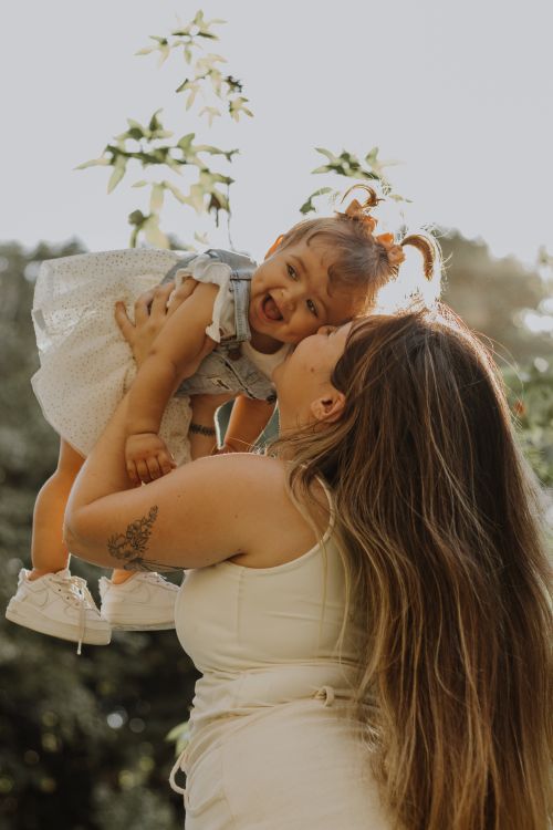 Free A loving mother lifts her joyful daughter in a sunny outdoor setting, showing a tender moment of happiness. Stock Photo