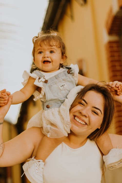 Free Smiling mother carrying her happy daughter on shoulders outside, capturing pure joy and love. Stock Photo