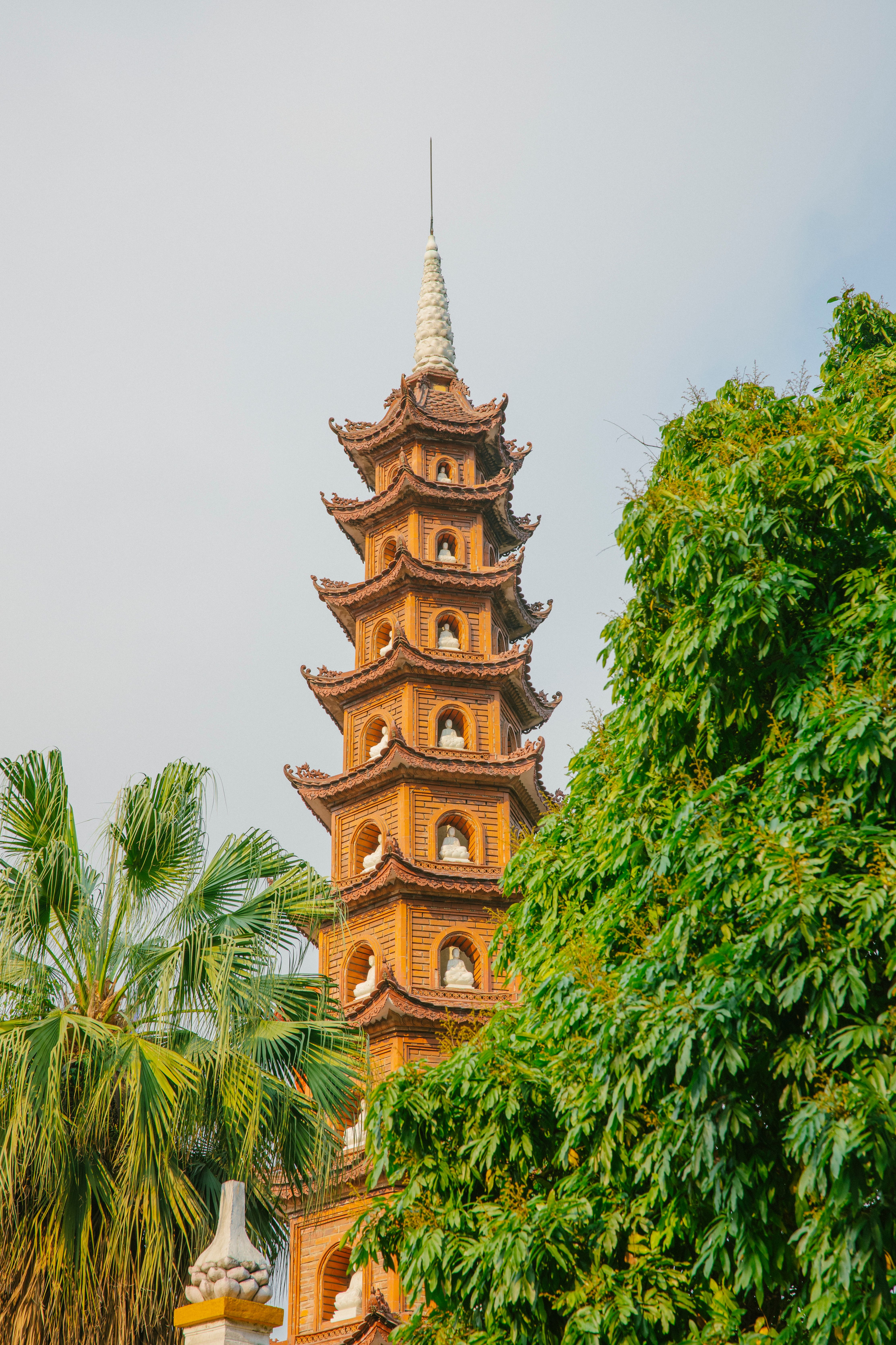 Tran Quoc Pagoda in Hanoi against a clear sky, amidst lush green trees, showcasing Vietnamese architecture.