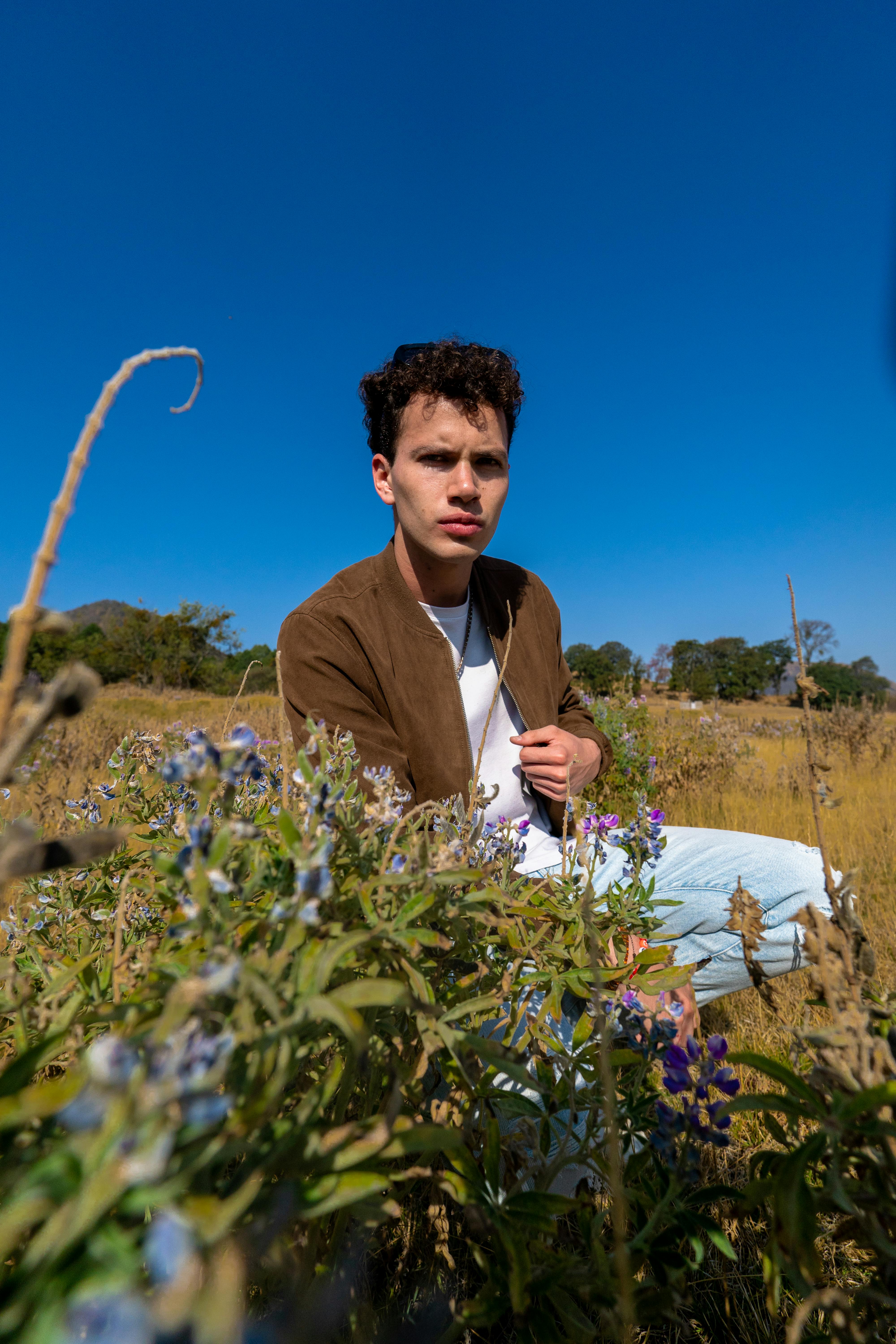 Man crouching in a vibrant field with wildflowers under a clear blue sky in Amecameca, Mexico.