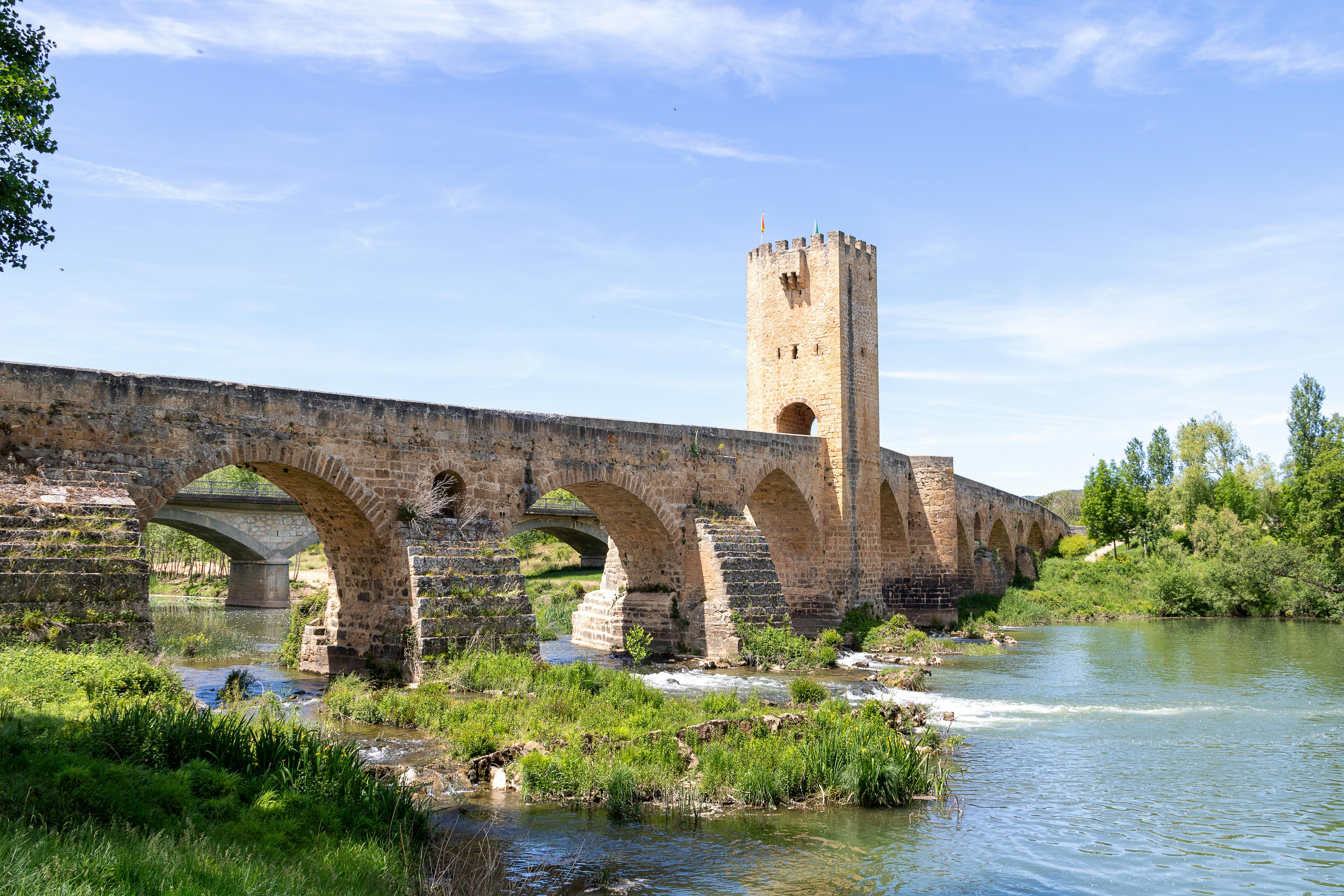 Ancient stone bridge spanning a river in Frías, Spain under a clear blue sky.