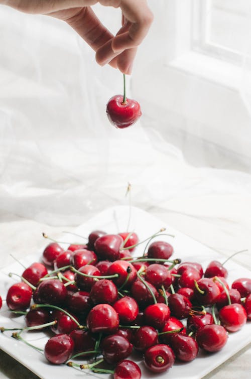 A person is holding a cherry on a plate