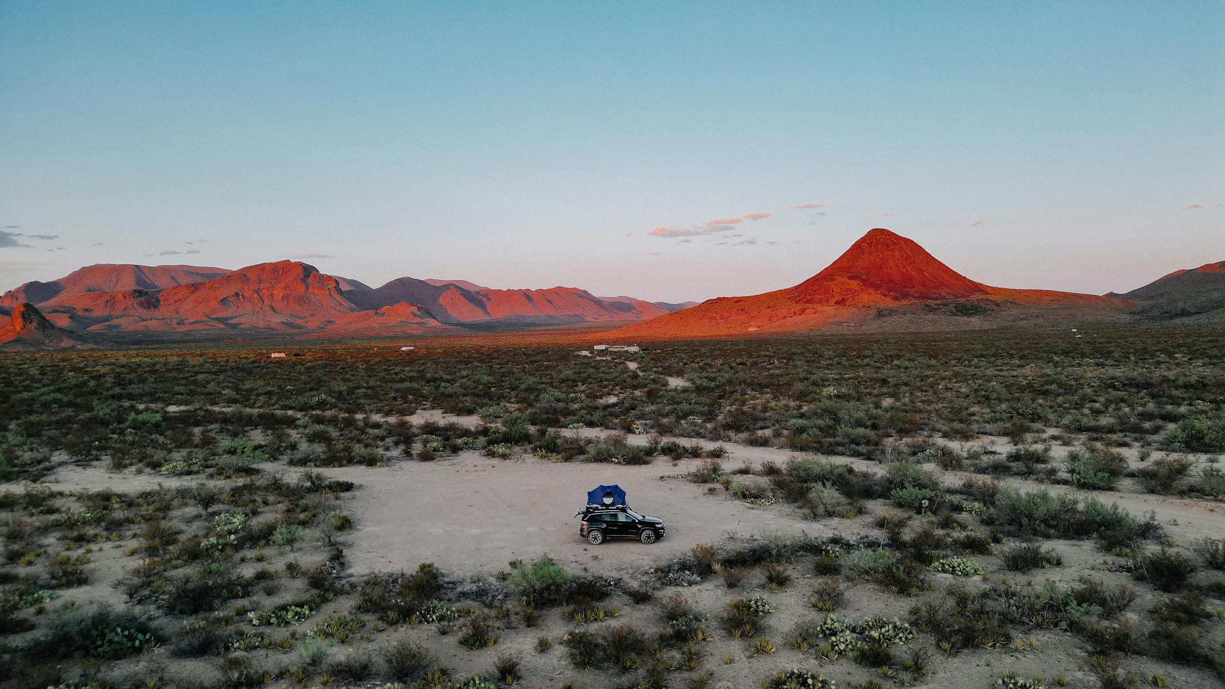 free photo of drone shot of a car parked in the middle of a desert with mountains in the distance