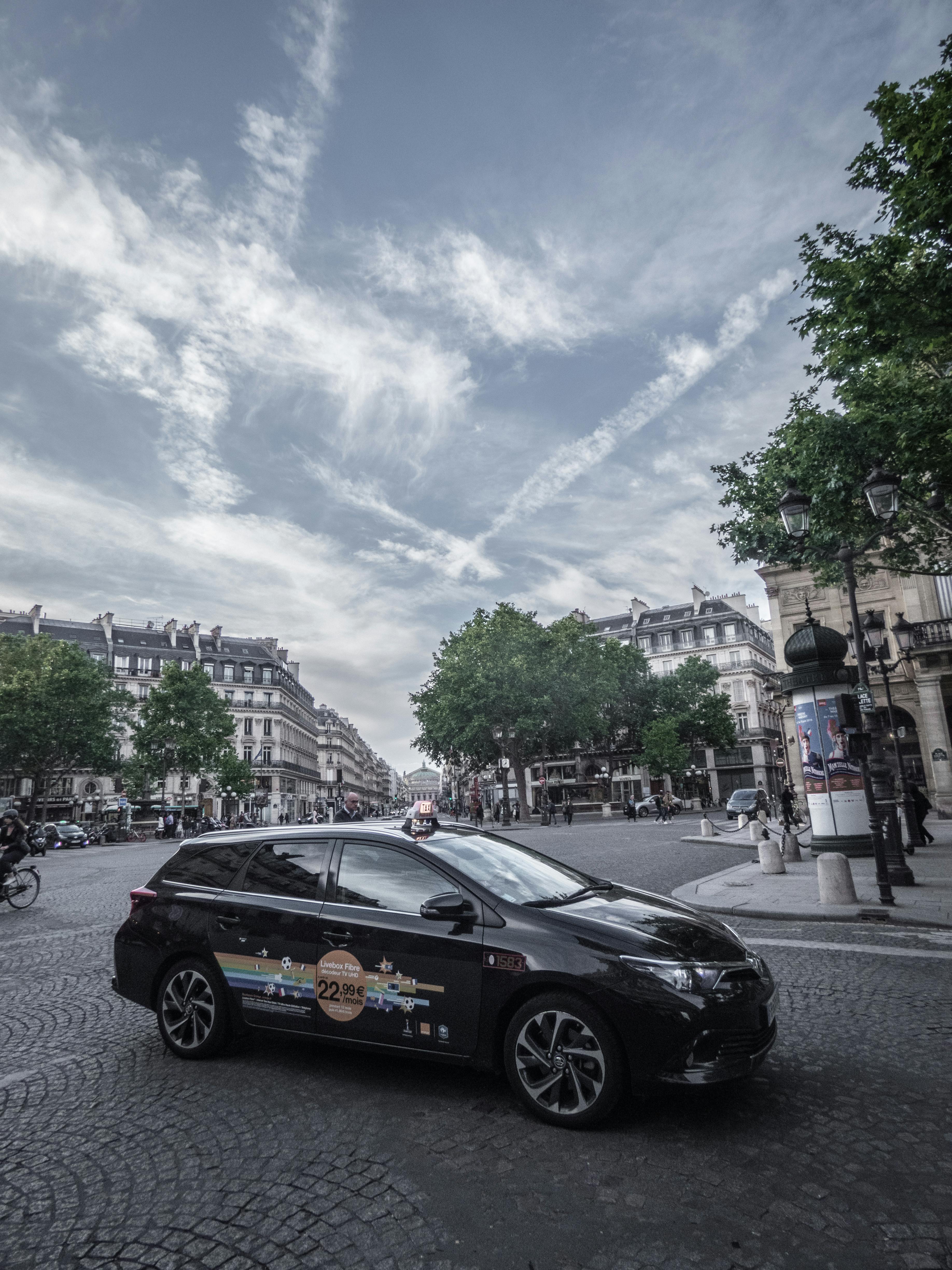 一辆时尚的黑色汽车停在巴黎的鹅卵石街道上，捕捉着城市生活与经典建筑的韵味