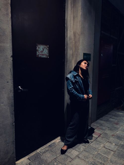 Free Moody urban portrait of a woman in casual wear under dim street lighting. Stock Photo