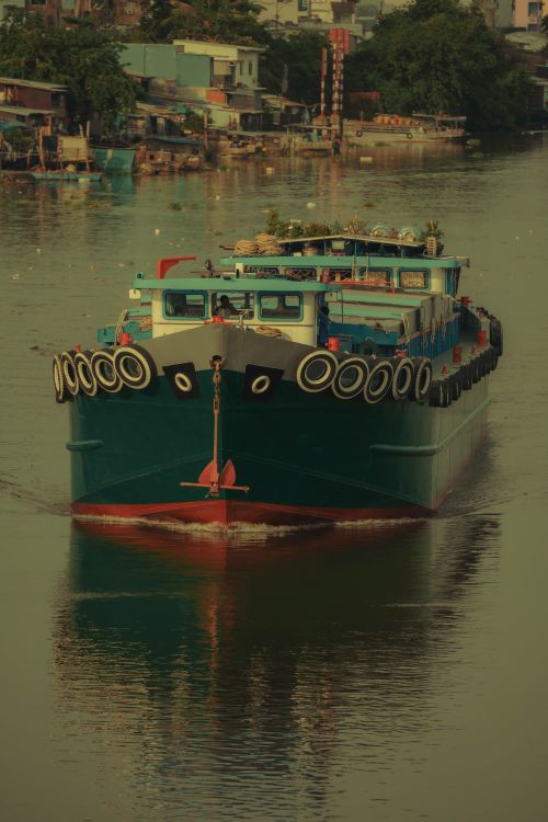 Free A vibrant cargo boat travels down a serene river with lush surroundings and reflections. Stock Photo