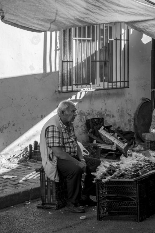 Free Elderly man sitting by crates in urban street market, black and white photo. Stock Photo