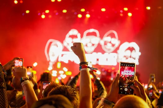 Vibrant concert atmosphere with fans capturing the stage on smartphones with raised hands.