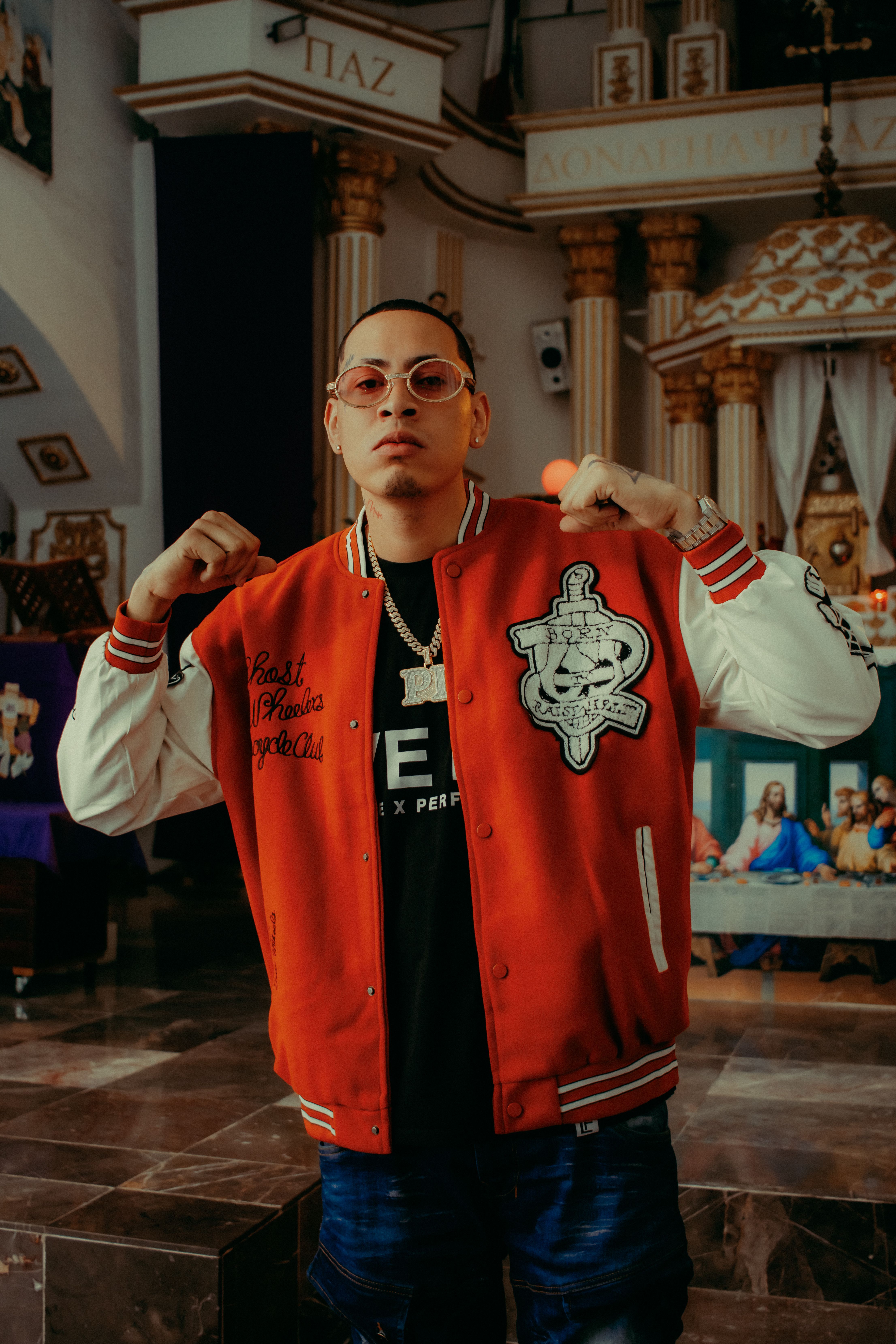 Portrait of a fashionable man standing inside a decorated church wearing a red jacket and glasses.