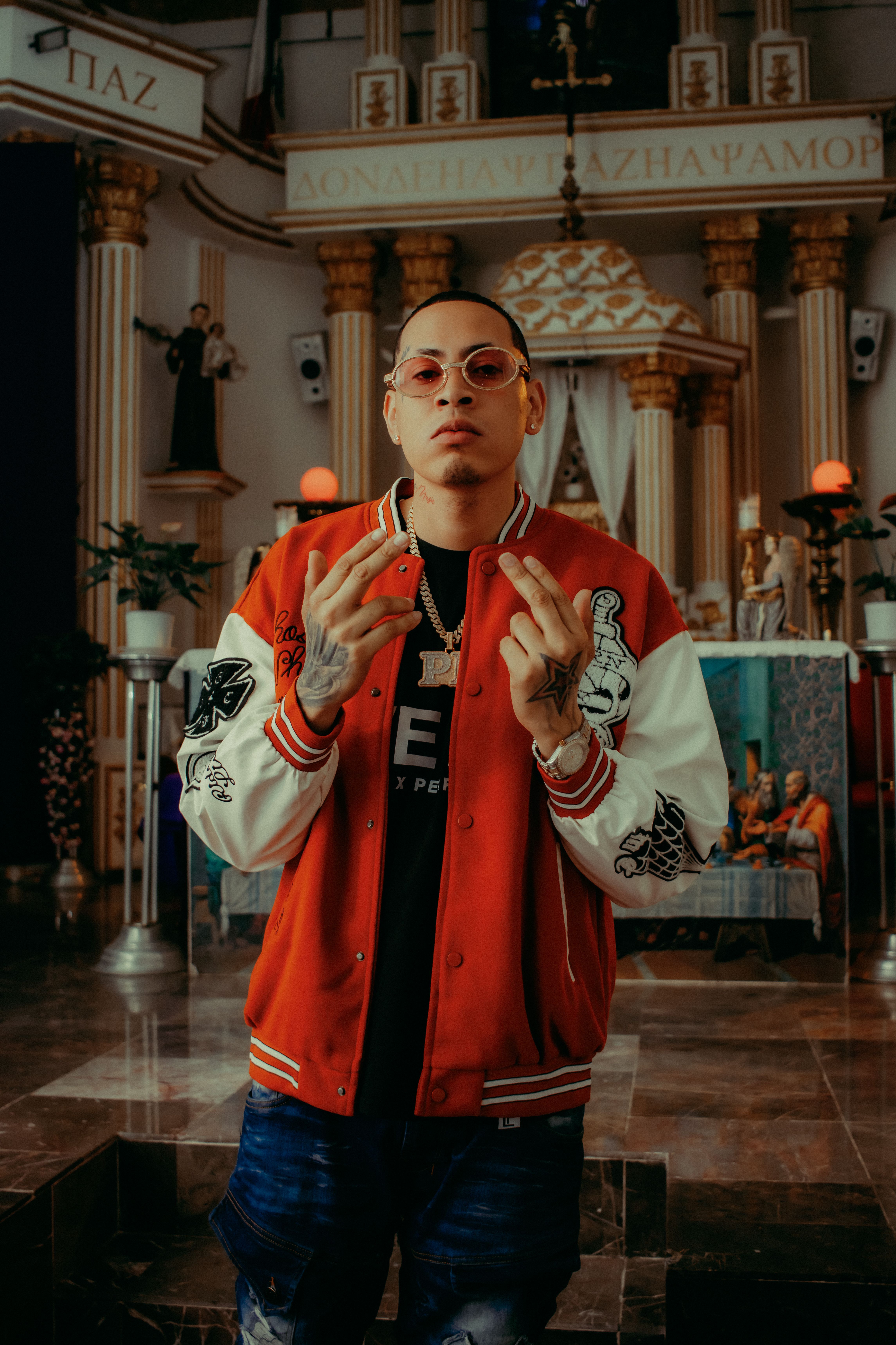 Stylish man in sunglasses and a baseball jacket posing inside a beautifully decorated church.