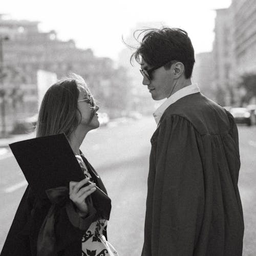A man and woman in graduation gowns standing on the street