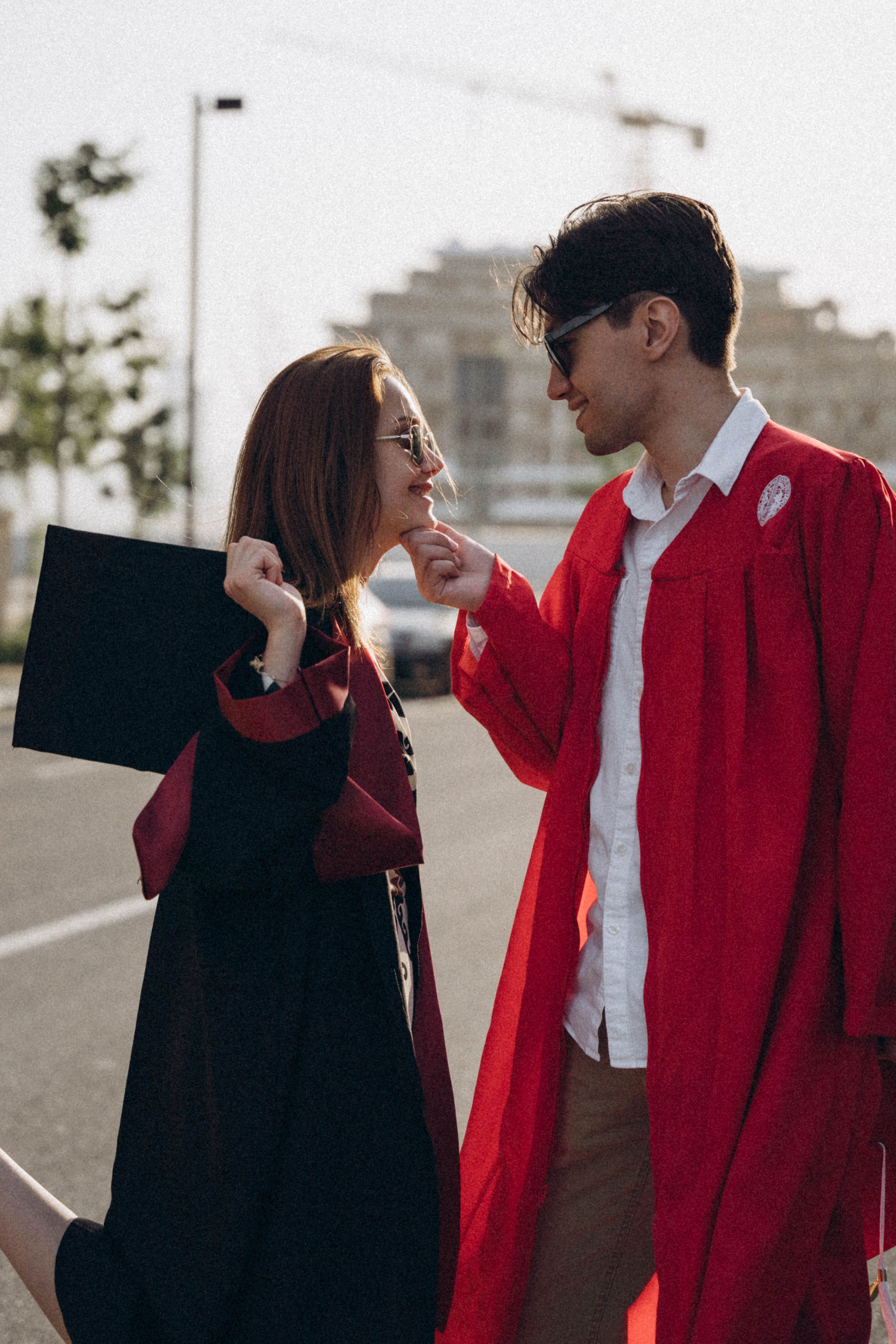 A joyful couple in graduation attire celebrating outdoors in a city setting.