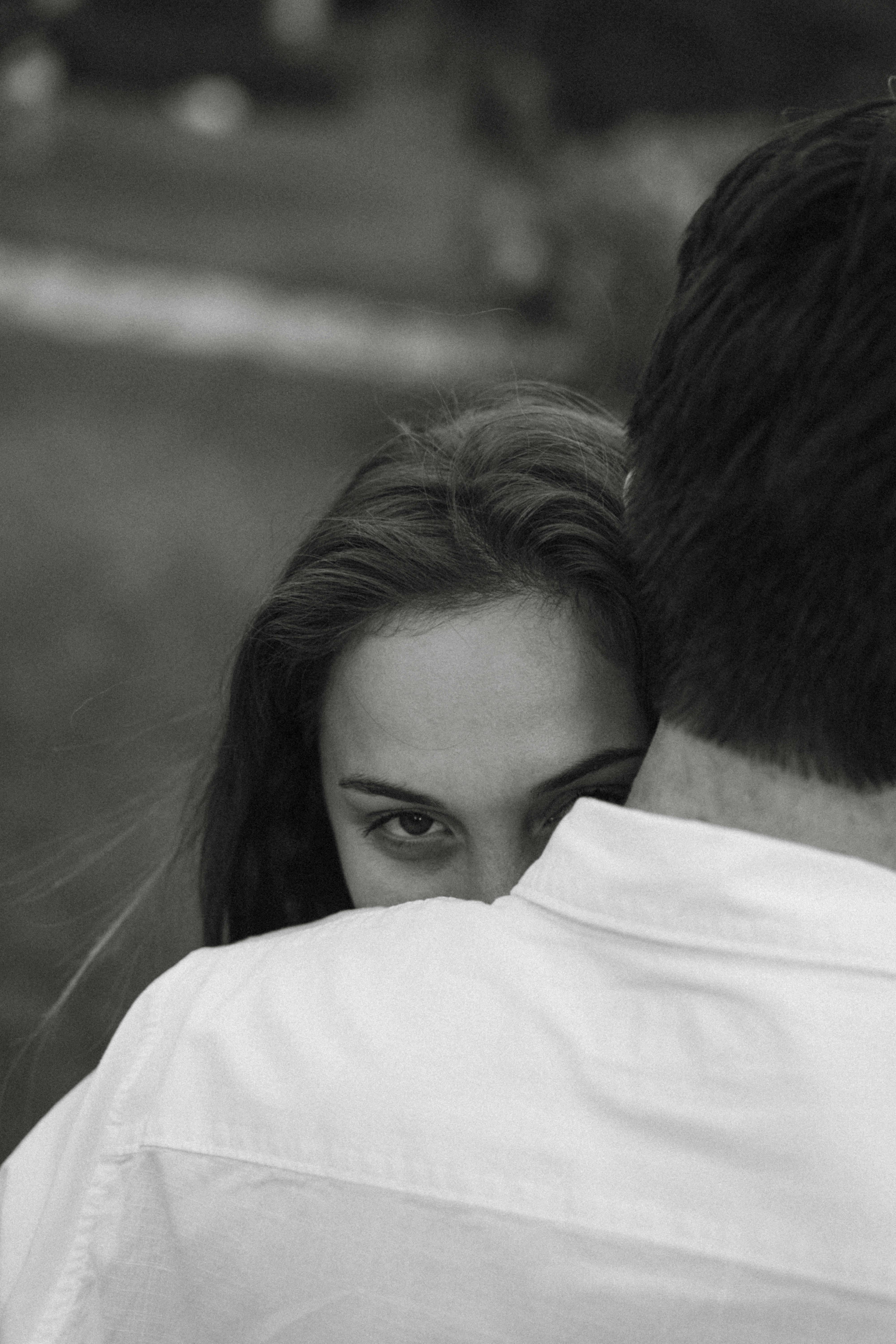 A close-up black and white portrait capturing a couple's intimate embrace outdoors.