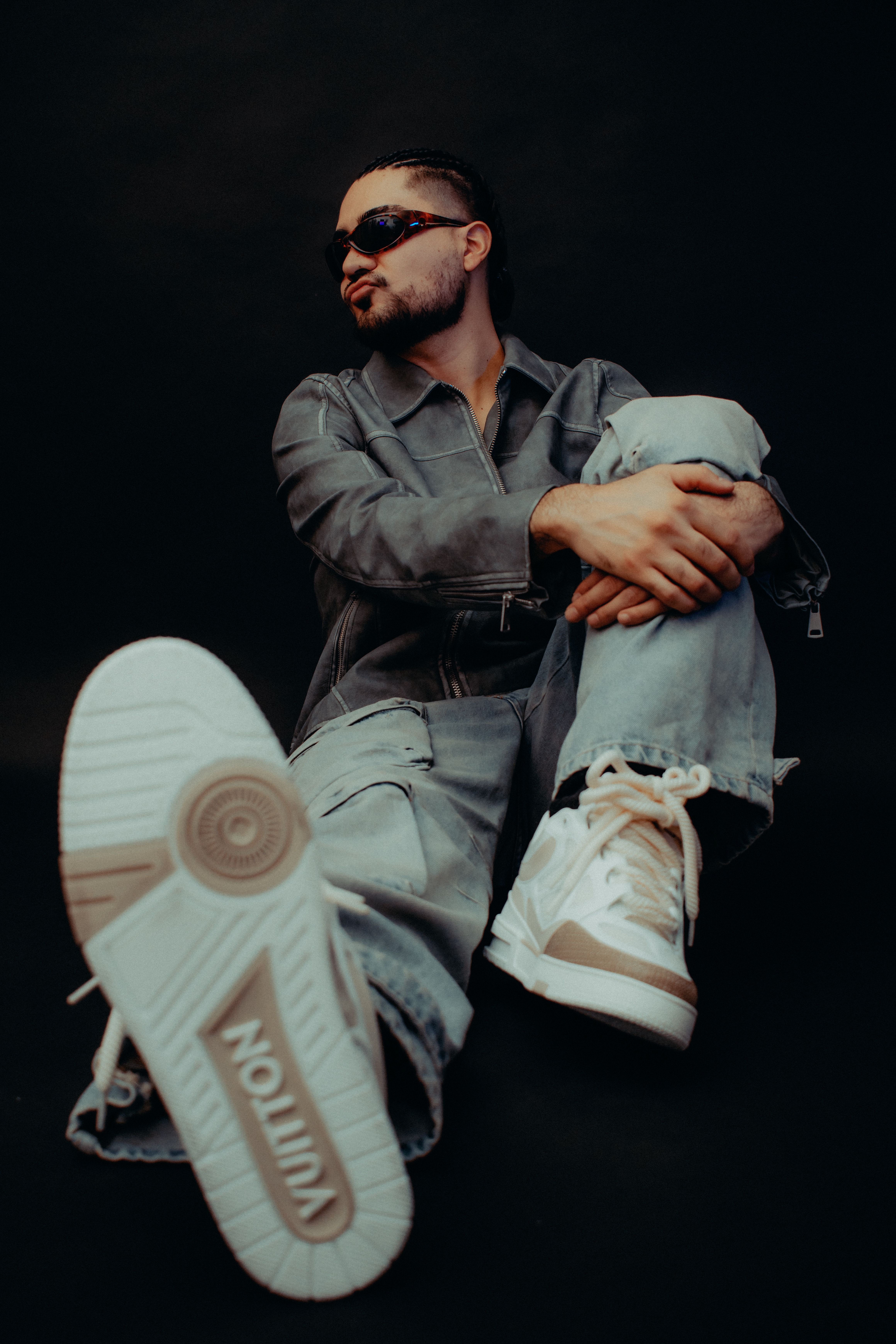 Model sitting in studio showcasing trendy designer sneakers and sunglasses with a bold style.