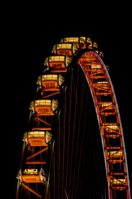 Brightly lit Ferris wheel cabins glow against a dark night sky.