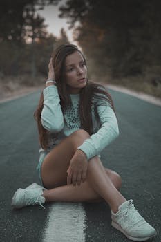 一位穿着休闲装的年轻时尚女子坐在森林小路上，看起来若有所思