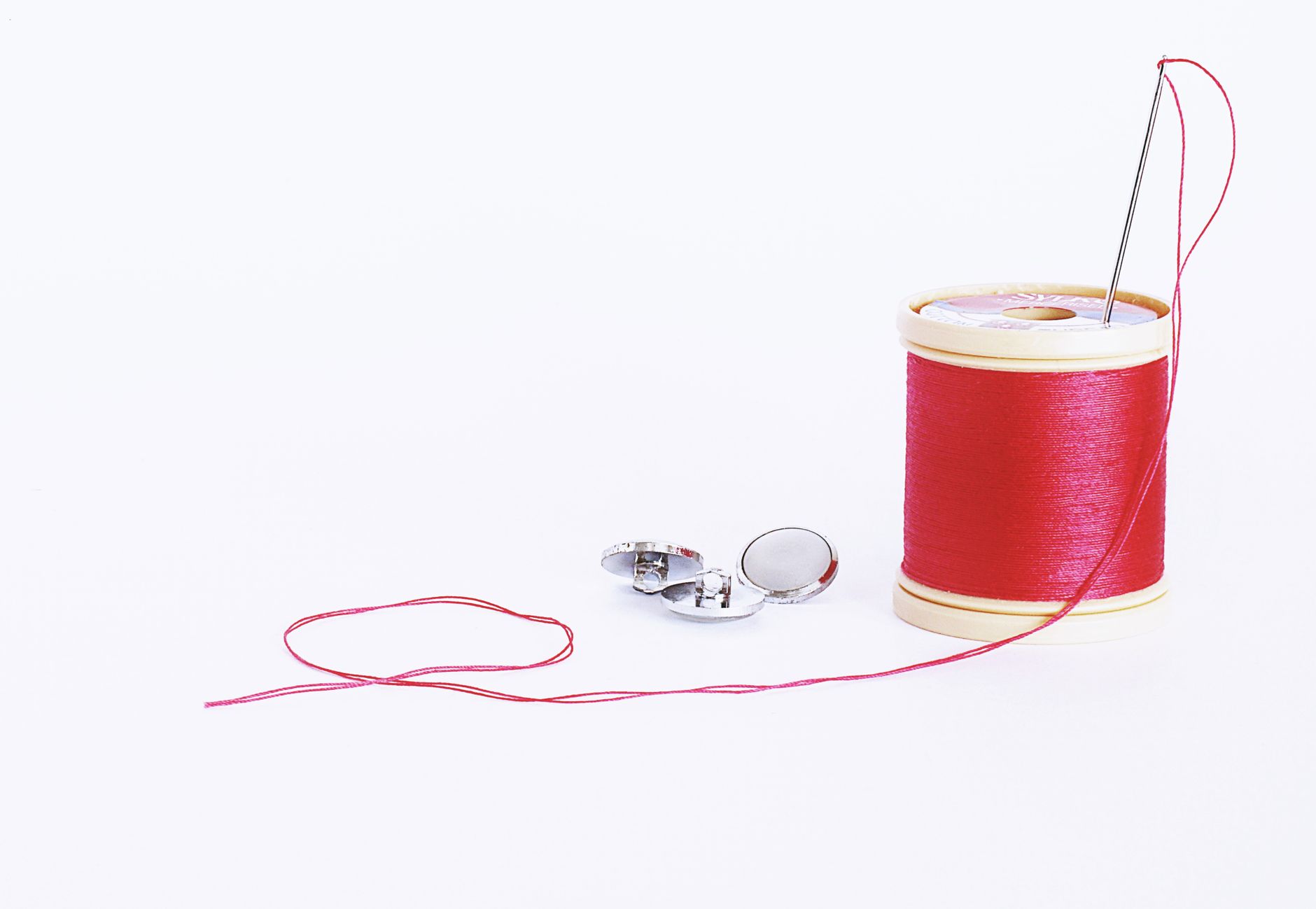 Close-up of red thread spool with needle and buttons, perfect for sewing projects.