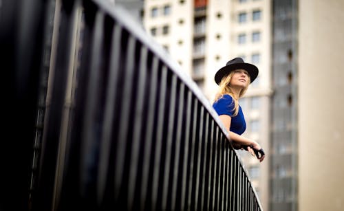 Free Woman wearing a blue top and a hat leaning on metal railing Stock Photo