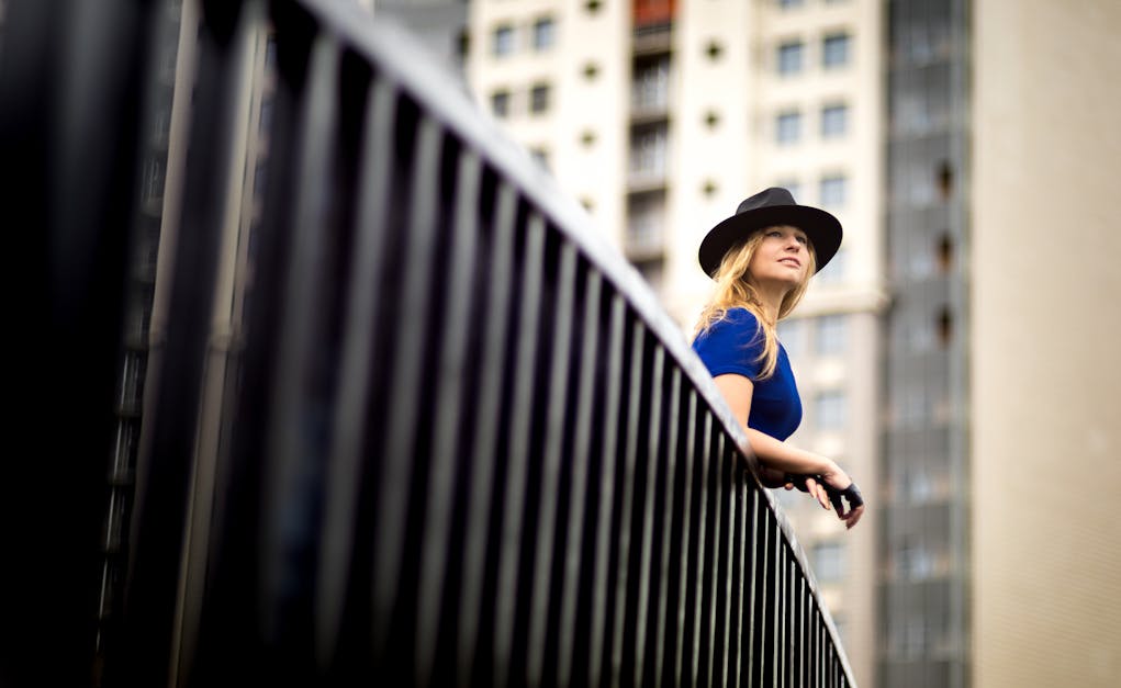 Woman wearing a blue top and a hat leaning on metal railing · Free ...