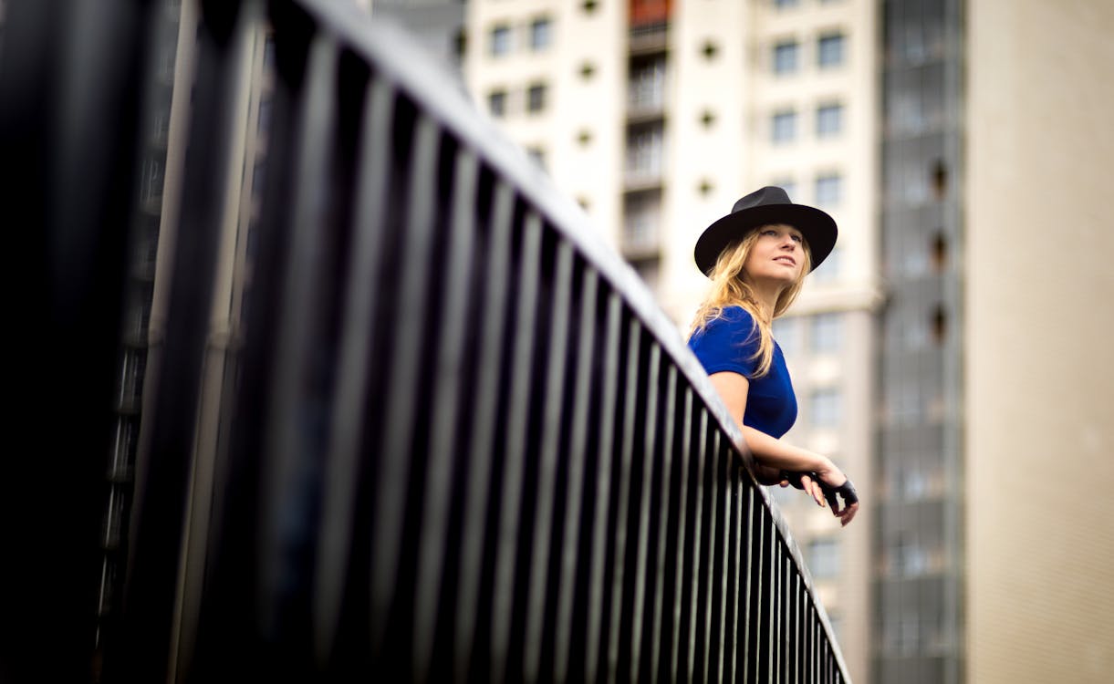 Free Woman wearing a blue top and a hat leaning on metal railing Stock Photo