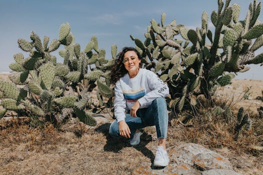 一张随意的照片里，一名妇女蹲在阳光明媚的干旱环境中，身旁是仙人掌植物
