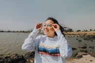 一名年轻女子在岩石海岸微笑着调整眼镜，享受阳光明媚的一天