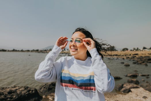 一名年轻女子在岩石海岸微笑着调整眼镜，享受阳光明媚的一天