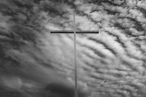 Free A striking black and white photo of a cross silhouetted against swirling clouds, evoking themes of spirituality. Stock Photo