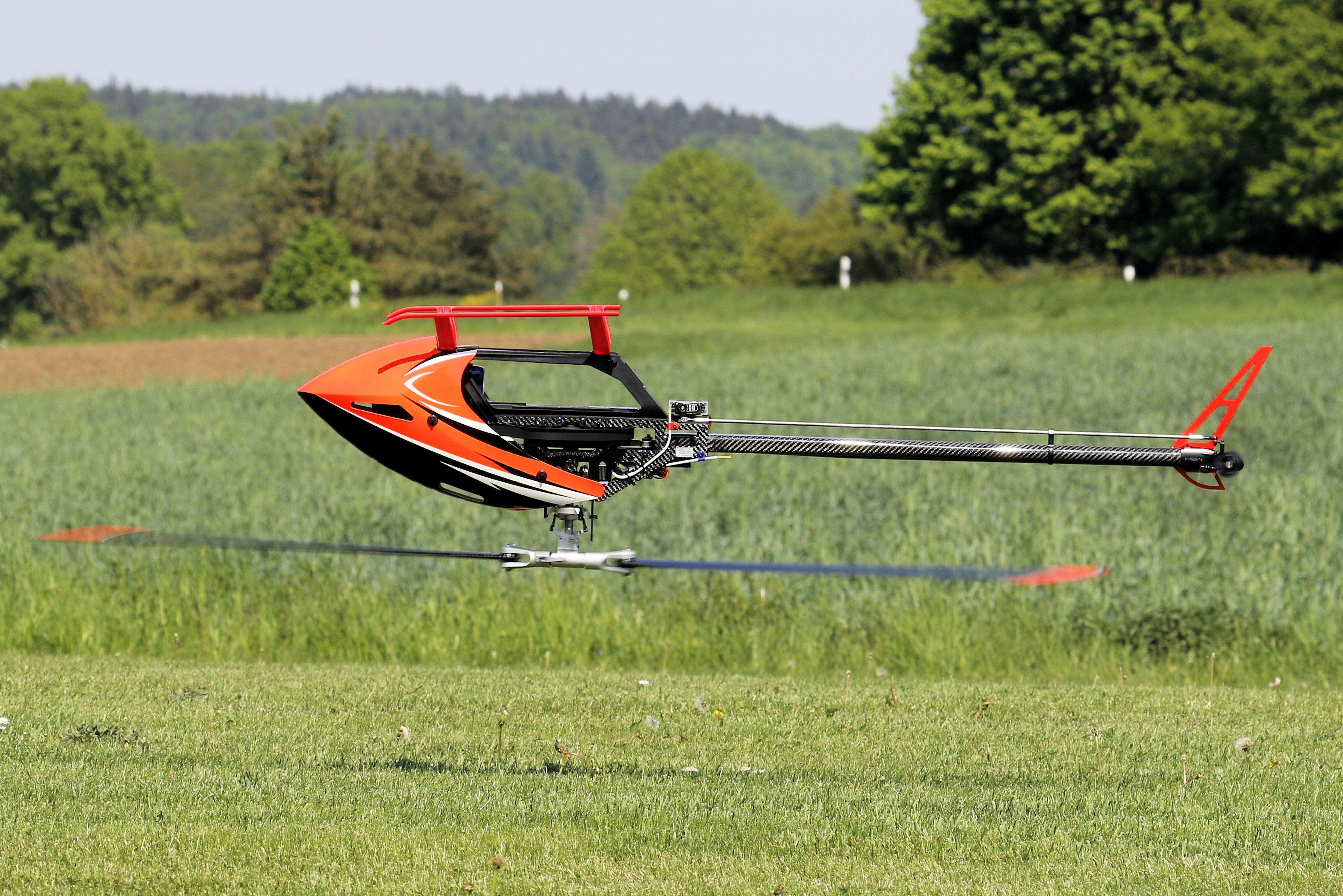 Orange remote control helicopter flying low over a grassy field in summer.