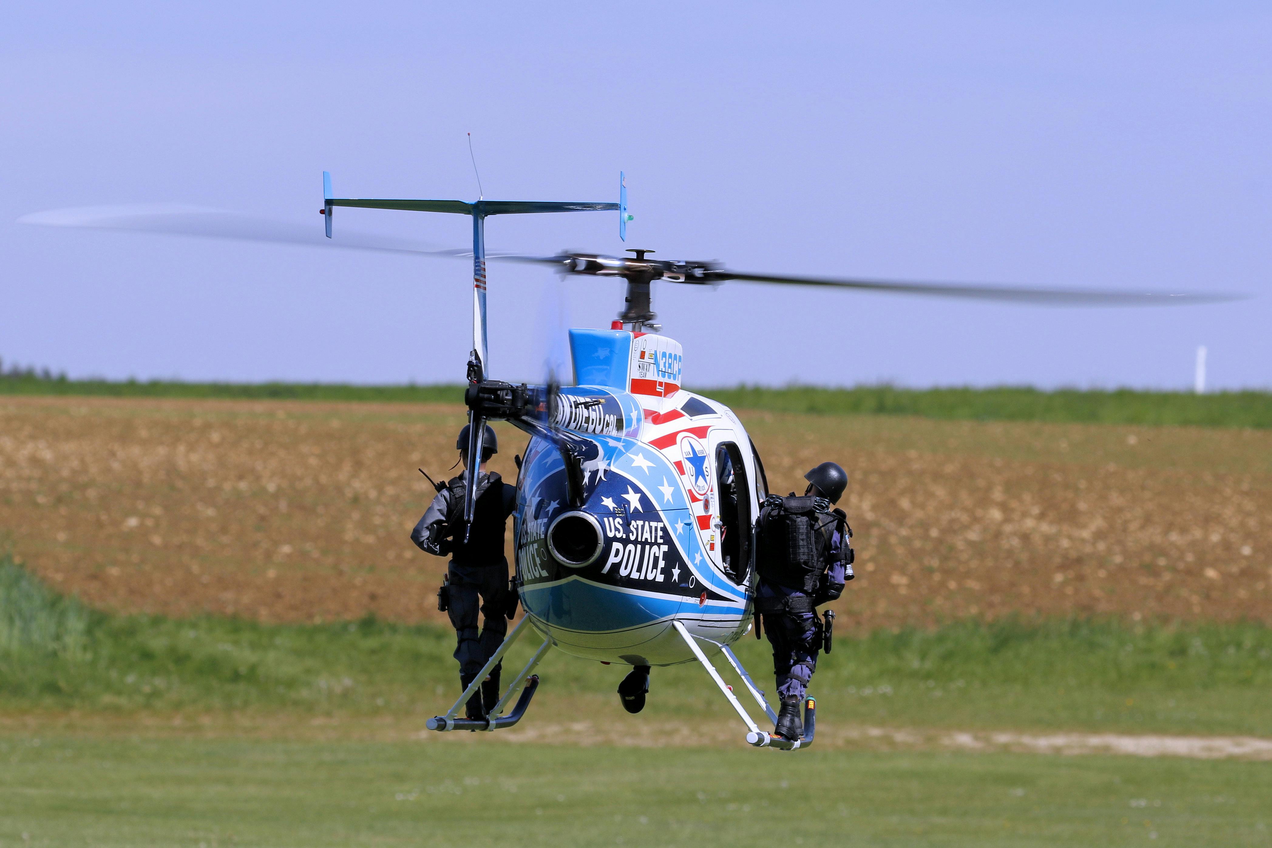 US state police helicopter with armed officers in a field, ready for deployment.