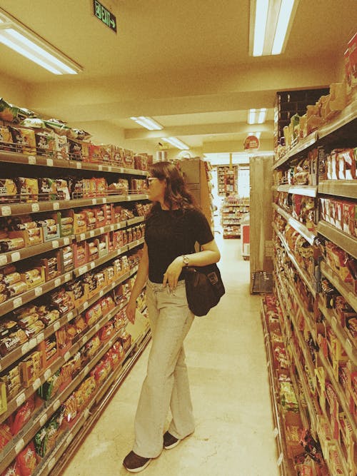 A woman is walking down a aisle in a grocery store