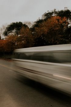 Dynamic photo capturing blurred motion of a vehicle speeding by autumn trees along a road.