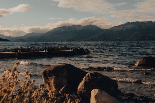 Free Mountain lake with rocky shore, pier, and waves at sunset. Stock Photo