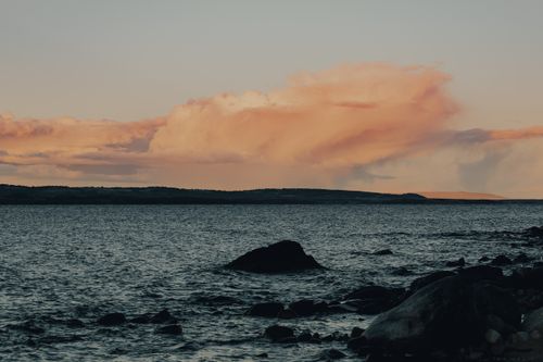 Free Serene ocean view at dusk with colorful clouds and rocky shoreline. Perfect for nature lovers. Stock Photo