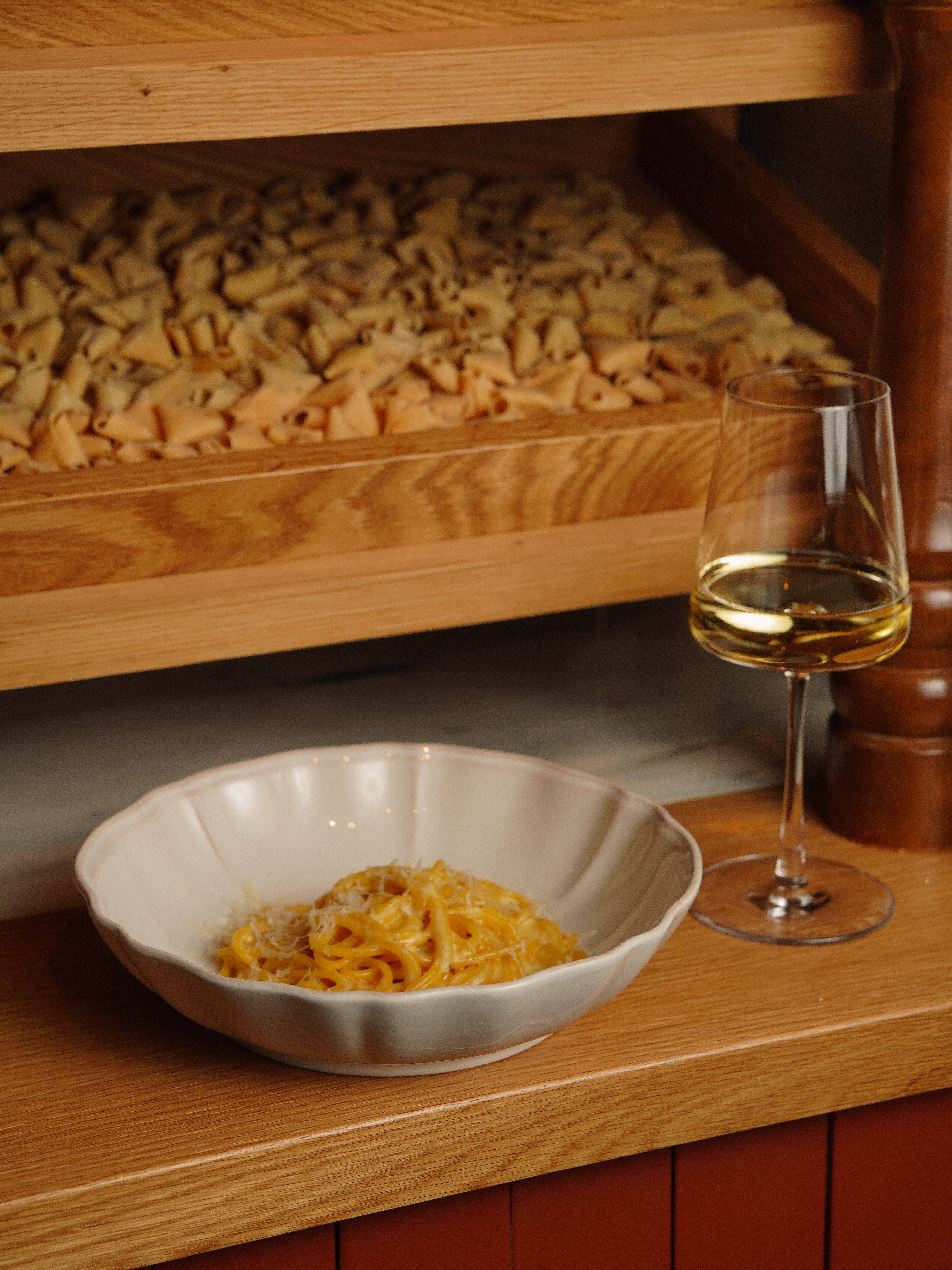 Indulge in a savory pasta dish paired with white wine, set against a rustic kitchen backdrop.
