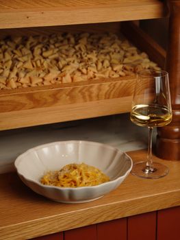 Indulge in a savory pasta dish paired with white wine, set against a rustic kitchen backdrop.