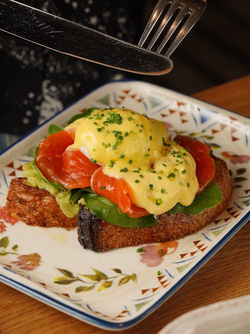 A person is holding a knife and fork over a plate of eggs benedict