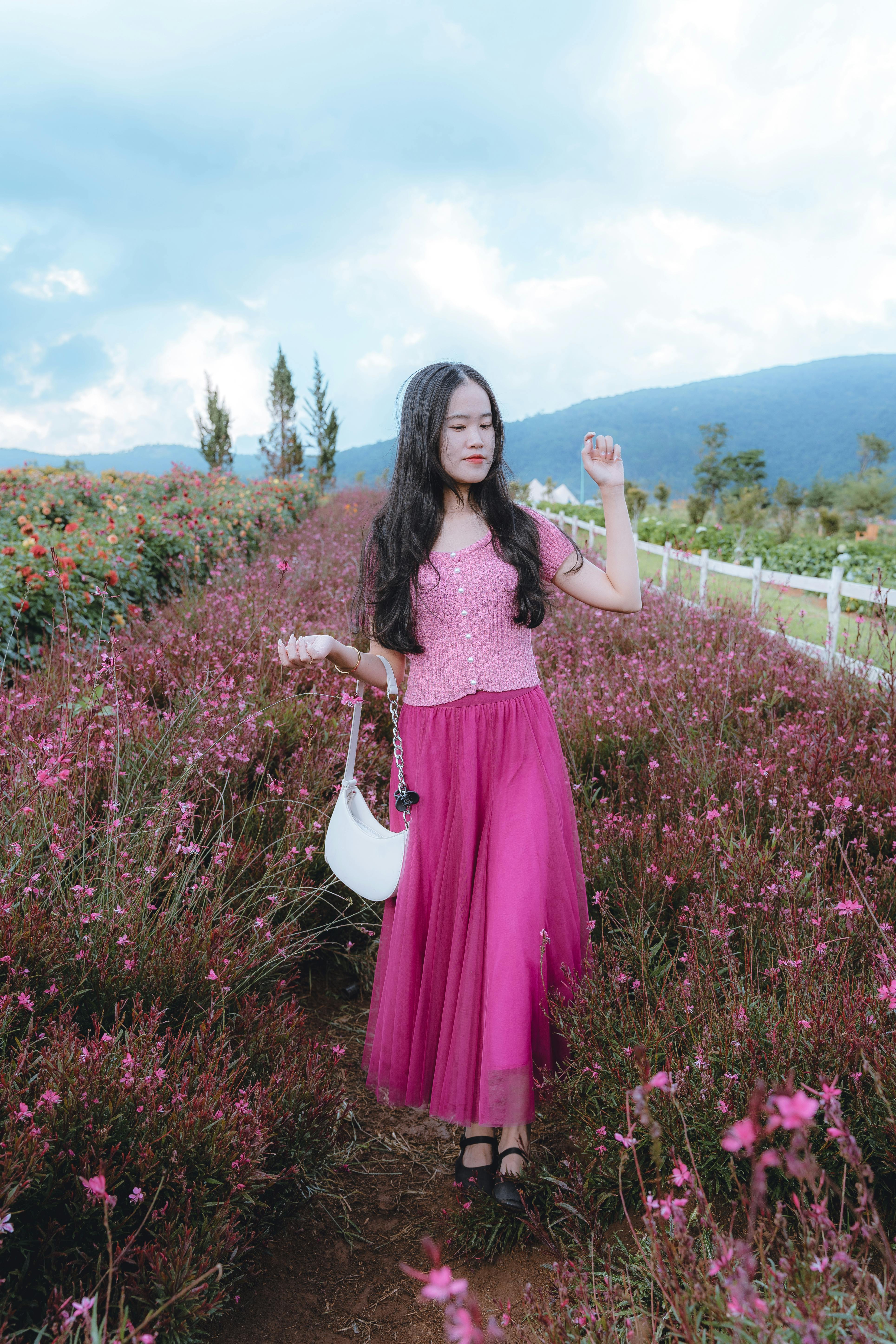 Asian woman in pink skirt standing in a vibrant flower field in Dalat, Vietnam, showcasing fashion and nature.