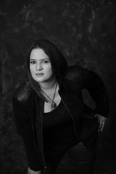 A striking black and white portrait of a woman wearing a leather jacket and pendant necklace.