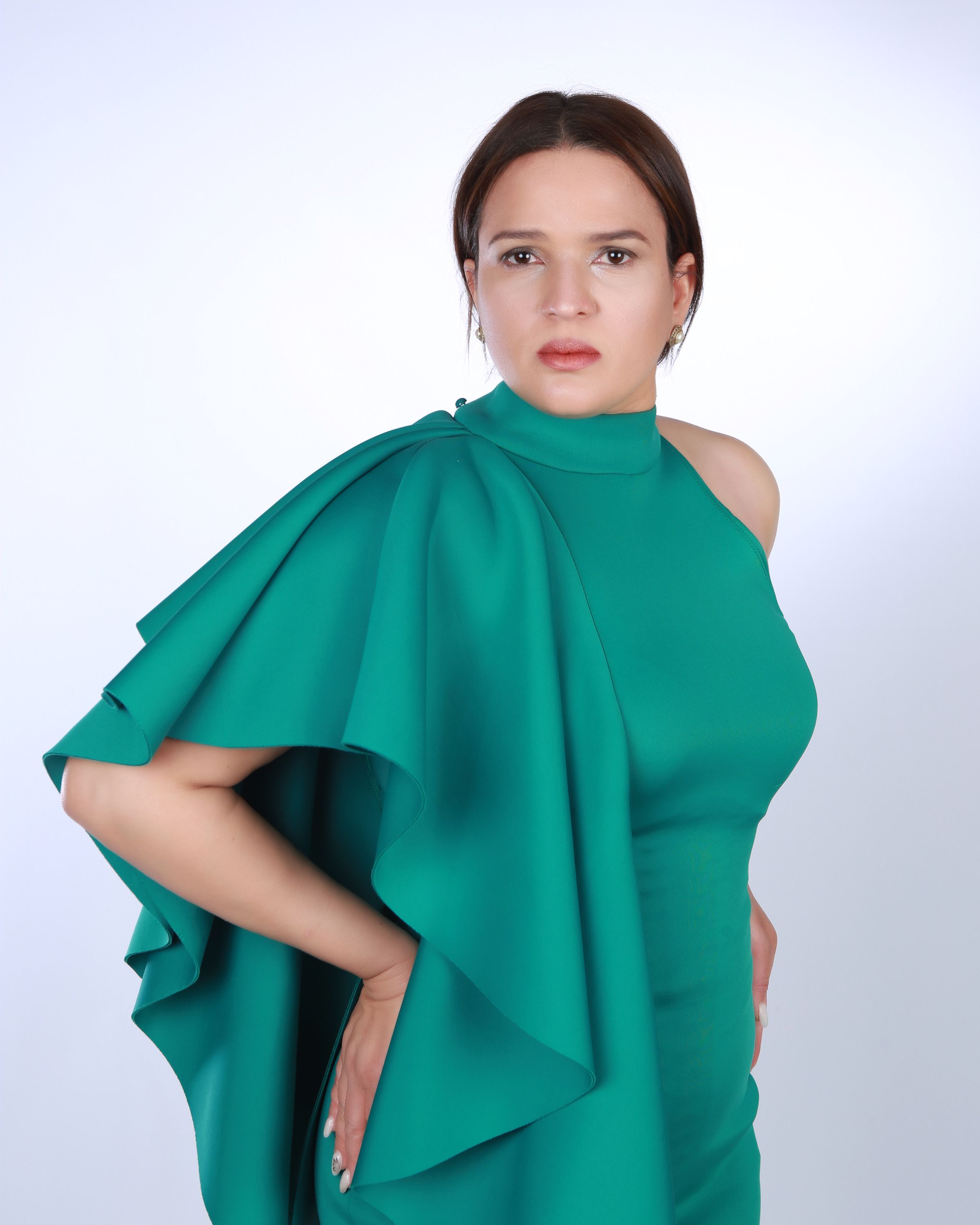 Fashion model in a green dress poses with hands on hips against white background.