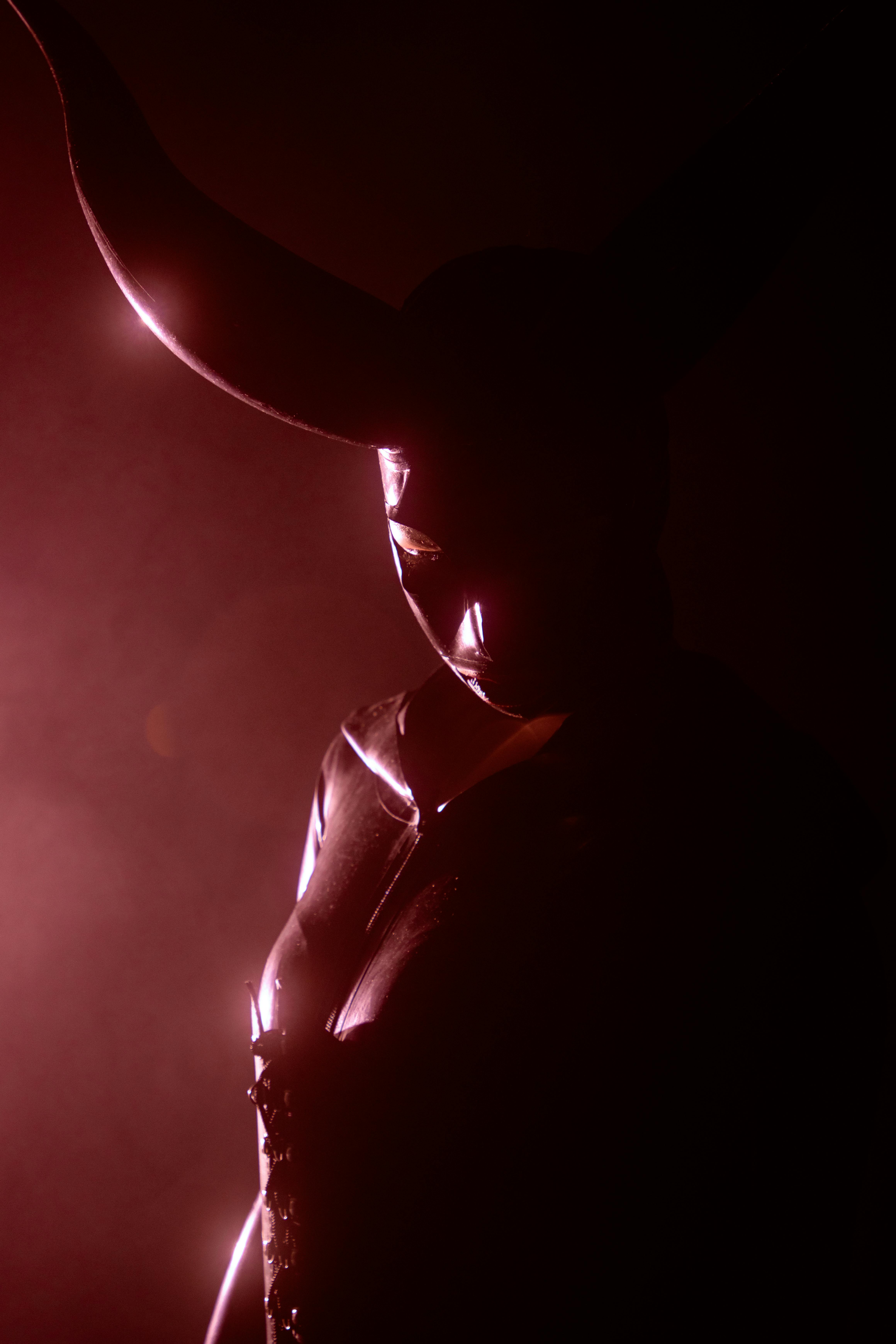 grátis Uma figura sombria usando uma máscara com chifres, iluminada por uma dramática luz vermelha. Foto profissional