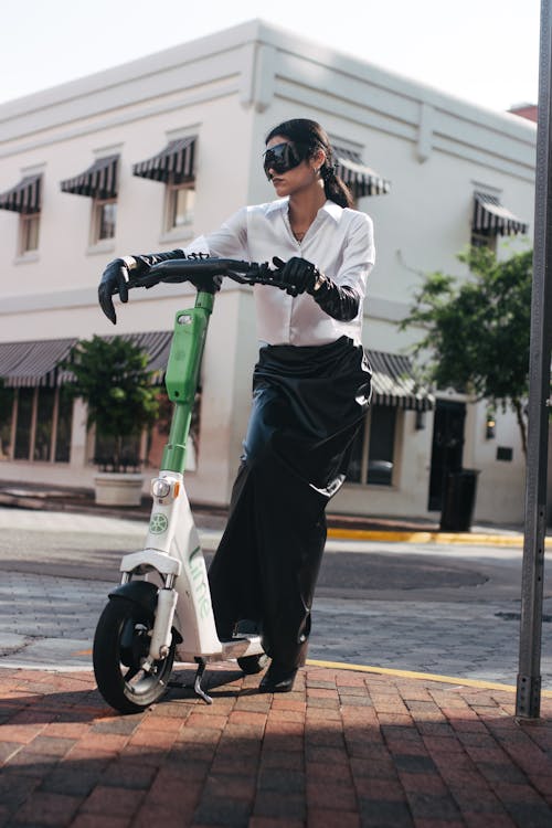 A woman in a skirt and sunglasses riding a scooter
