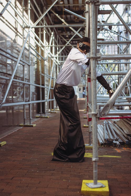 A man in a white shirt and black pants is standing on scaffolding