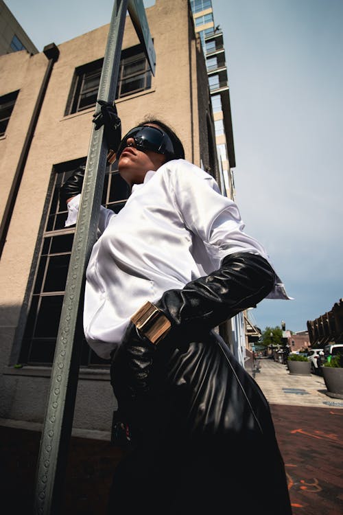 A woman in leather gloves and a white shirt leaning against a pole