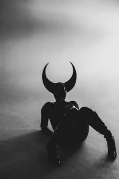 Black and white photo of a person in a devil costume with horns, lying down in a studio setting.