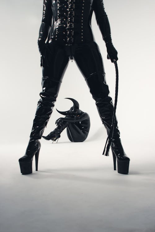 A woman in latex and boots posing with a whip