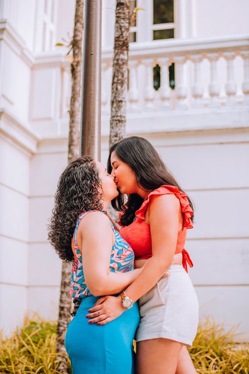 Free A happy couple embracing and sharing a kiss in a sunlit courtyard. Perfect for LGBTQ+ relationship themes. Stock Photo