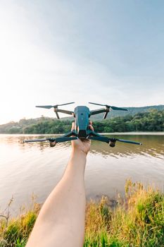A person holding a drone over a calm river with scenic greenery, showcasing rural tranquility and technology.