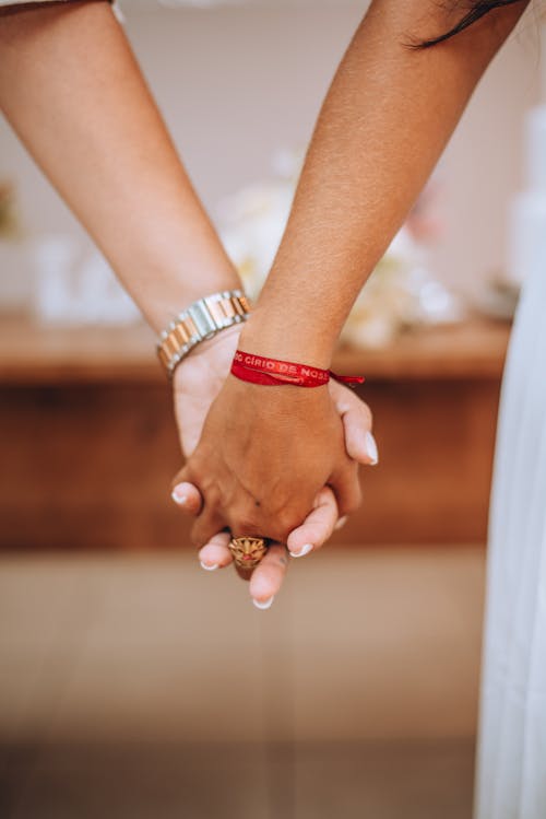 Two people holding hands with red bracelets