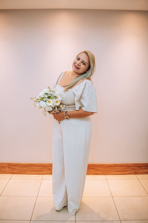 A woman in a white jumpsuit holding a bouquet